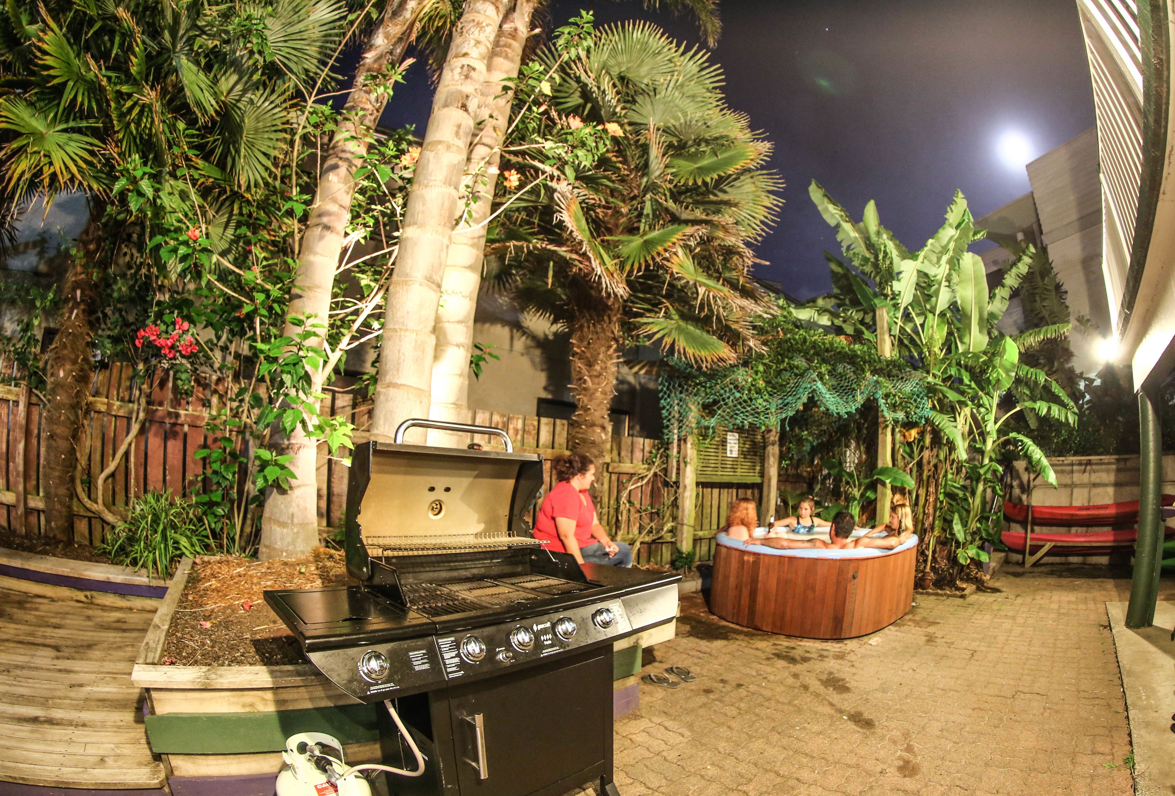 Een achtertuin met een barbecue, een hottub en weelderige tropische planten.