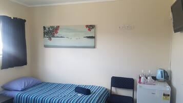 A bedroom with a bed, a chair, a small table with a kettle, a coffee maker, and a painting on the wall.