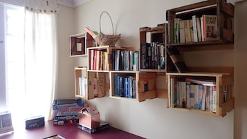 Una habitación con una estantería de madera llena de libros y una pequeña cesta. También hay cajas de Star Wars y LEGO sobre la mesa.