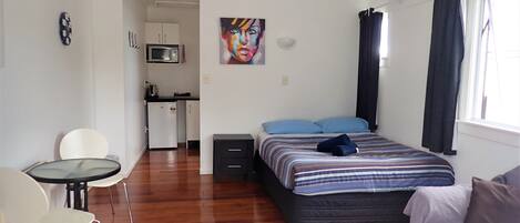 Habitación de hotel pequeña con cama, un escritorio, una silla, microondas, refrigerador y un cuadro en la pared.
