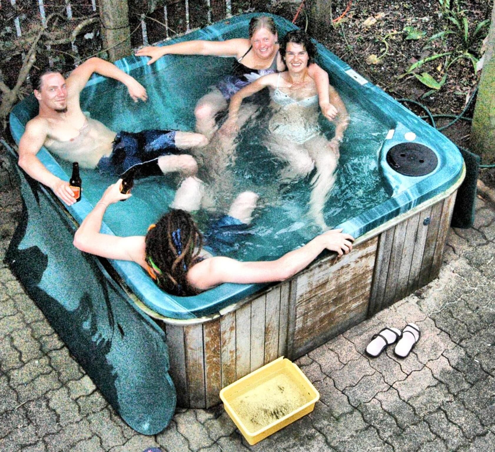 Un jacuzzi con cuatro personas, una botella y un par de zapatillas en el suelo.