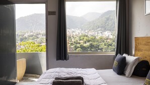 A hotel room with a bed, a window with a view of a city and mountains, a sign prohibiting smoking and drinking, and a suitcase on the bed. - Riverside home by bunkstay (Yamkeshwar)