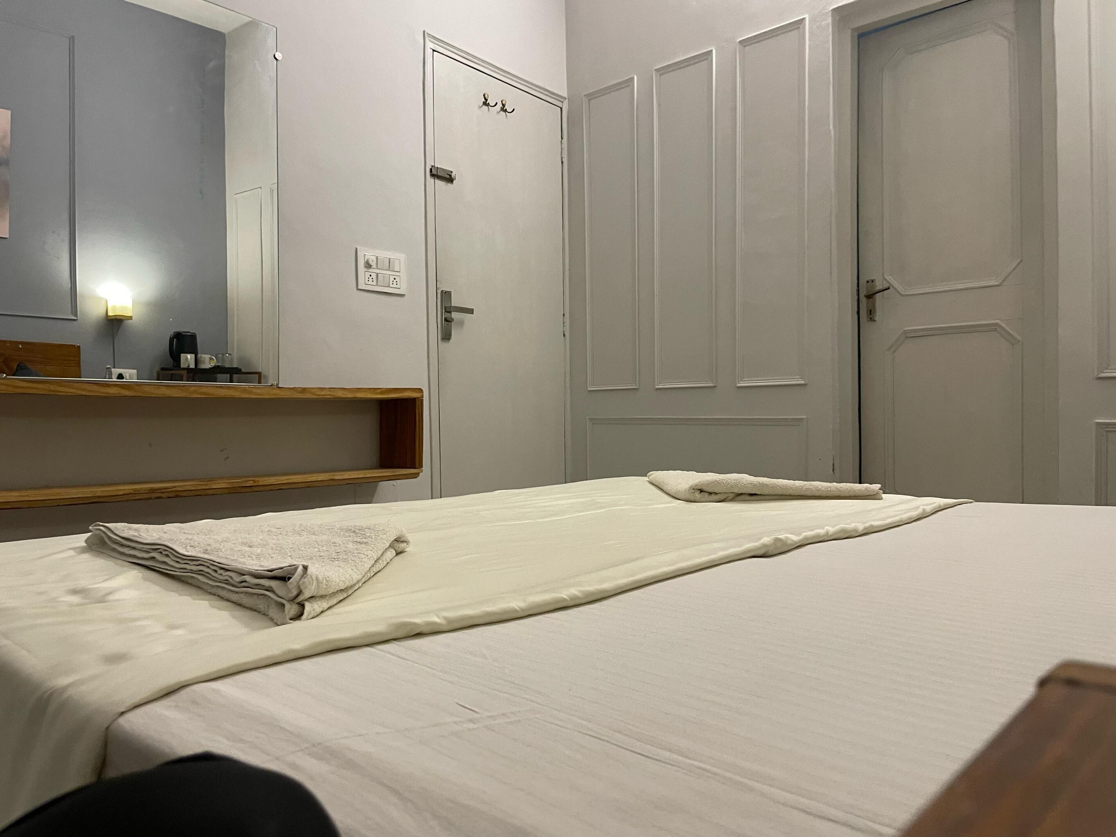 A hotel room with a bed, a wooden shelf, a mirror, and a door.