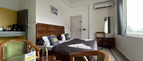 Une chambre d’hôtel avec un lit en bois, un bureau, une chaise, une petite table et une fenêtre avec des rideaux.