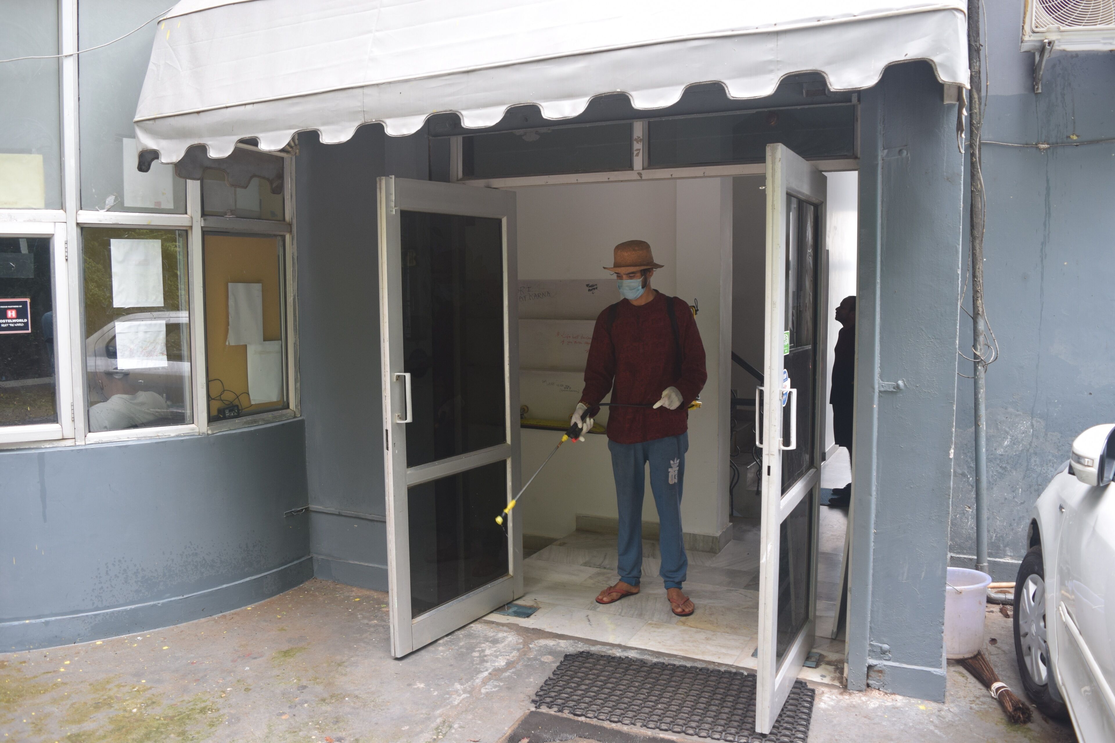 A person standing at the entrance of a building with a white awning, a door, and a window.