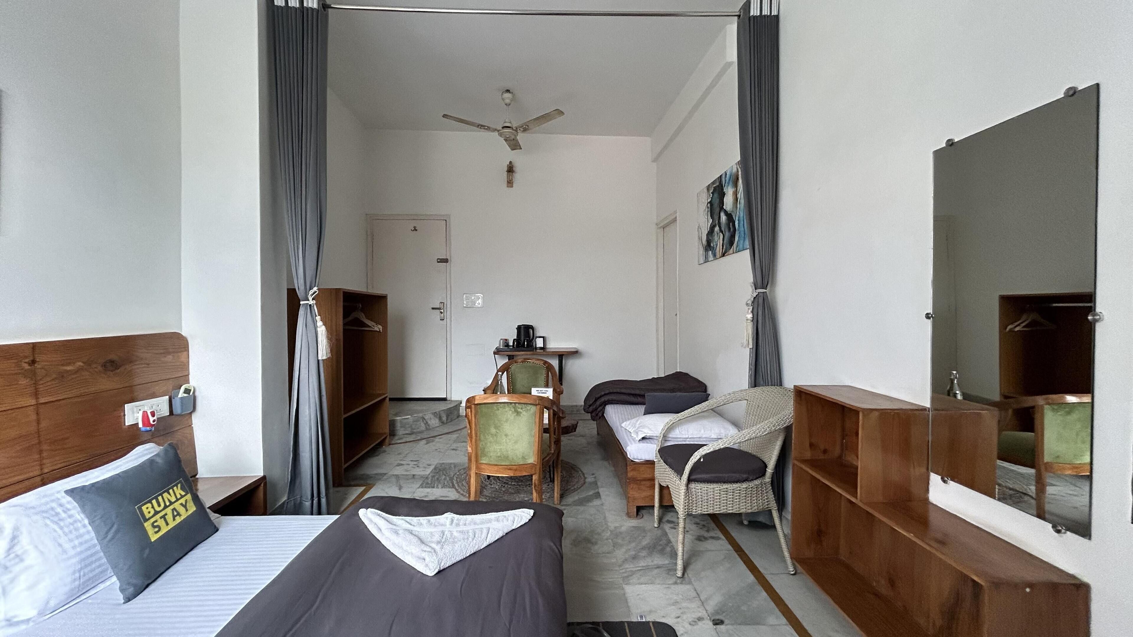 A hotel room with a bed, a chair, a small table with a coffee maker, a mirror, and a door leading to another room.
