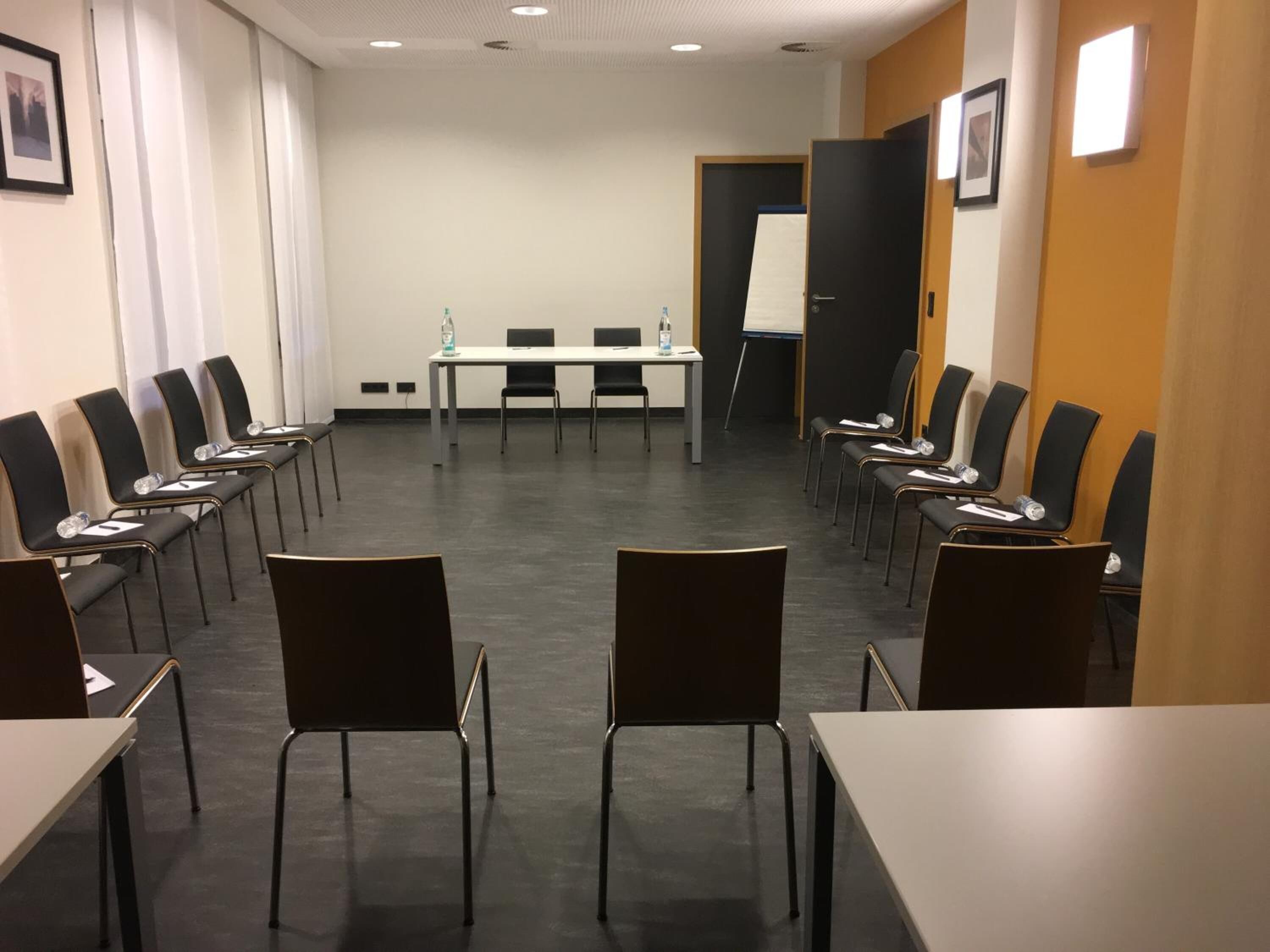 Un salón de conferencias con una larga mesa y sillas, una pizarra y cuadros en las paredes.