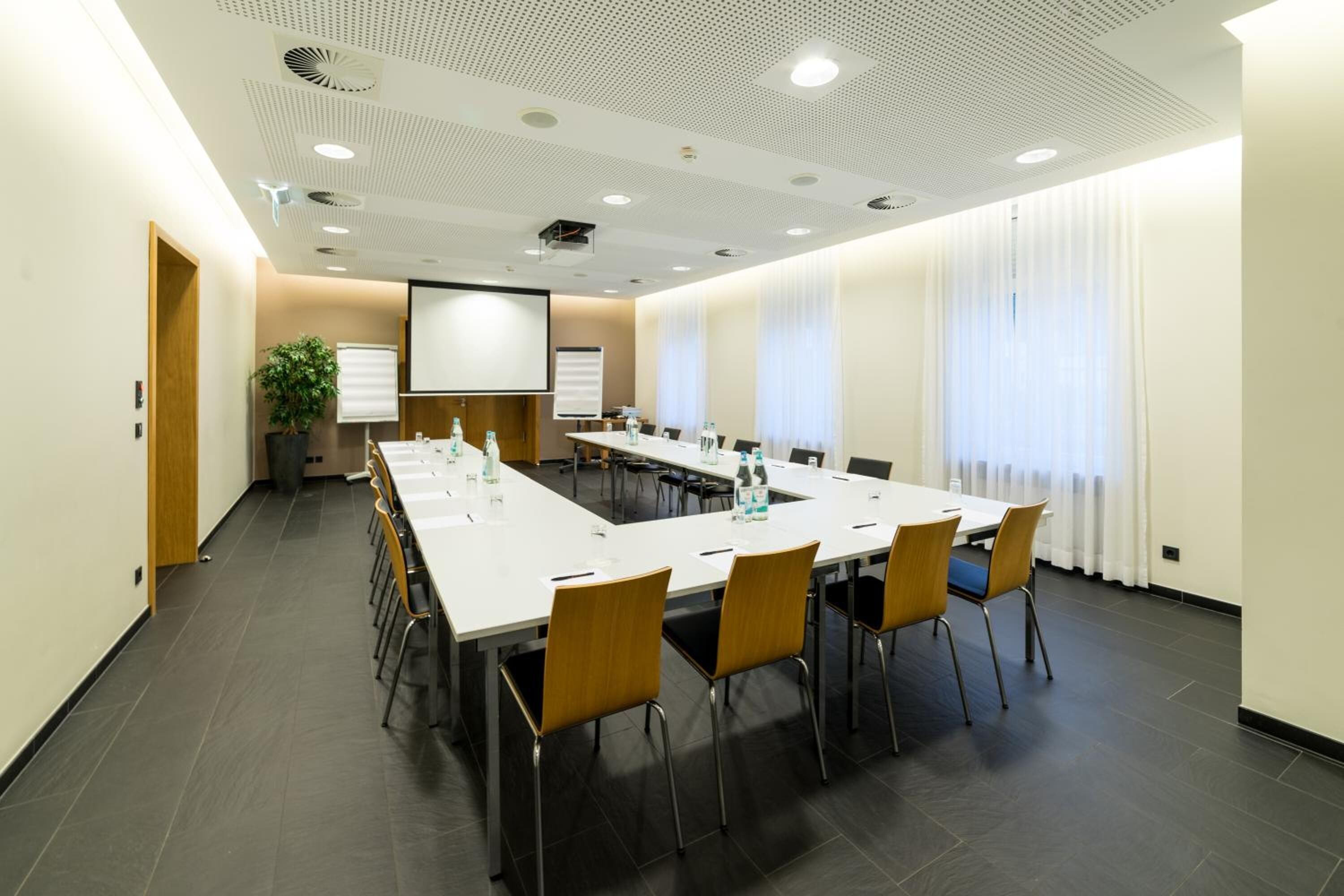 A conference room with a long table, chairs, a projector screen, and a whiteboard.