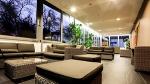 Un área de descanso moderna con mobiliario de mimbre, ventanas amplias y plantas de interior.