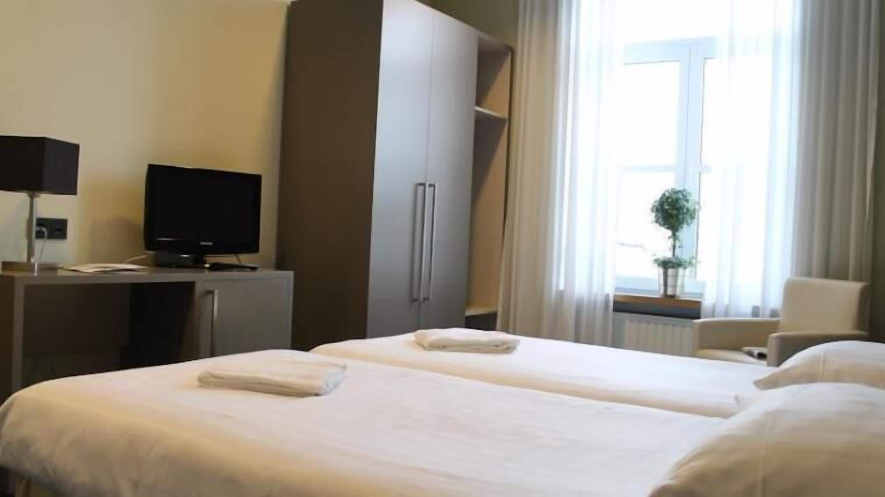 A hotel room with two beds, a desk with a computer, a television, and a window with curtains.