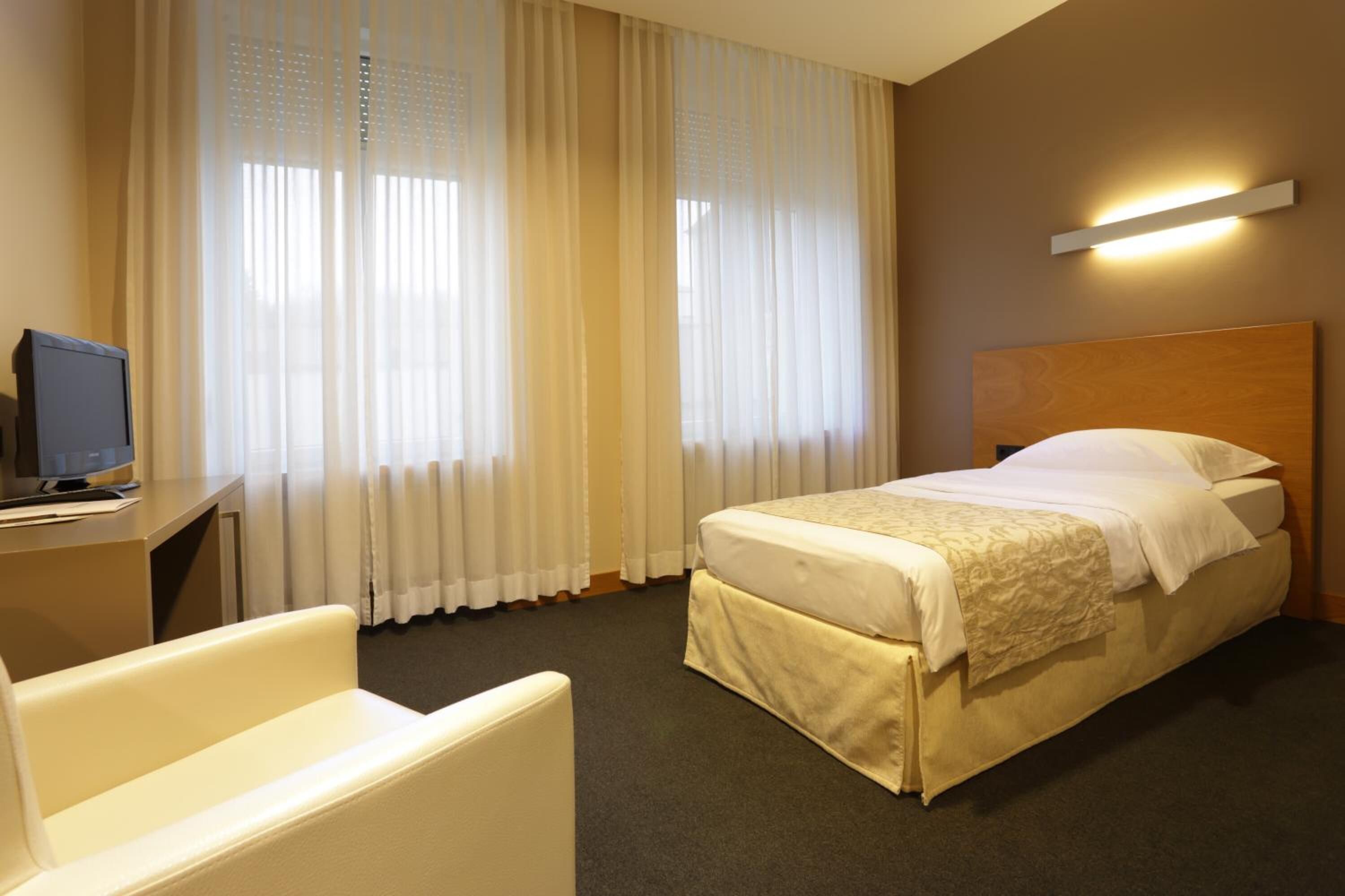 Ein Hotelzimmer mit einem Bett, einem Schreibtisch mit Computer und einem Stuhl.