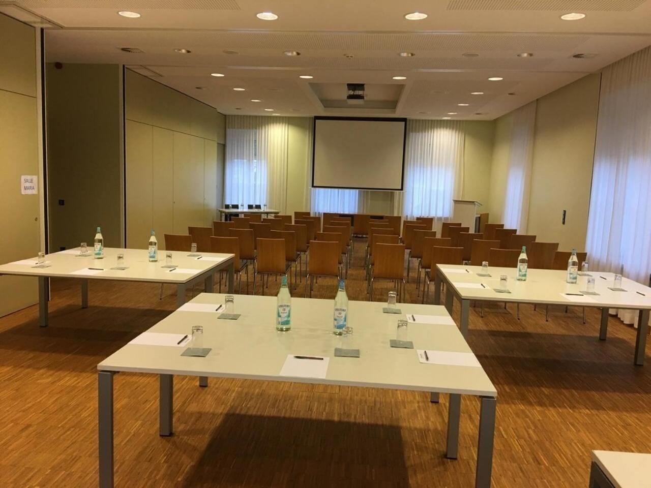 Un salón de conferencias con varias mesas, sillas y una pantalla grande.