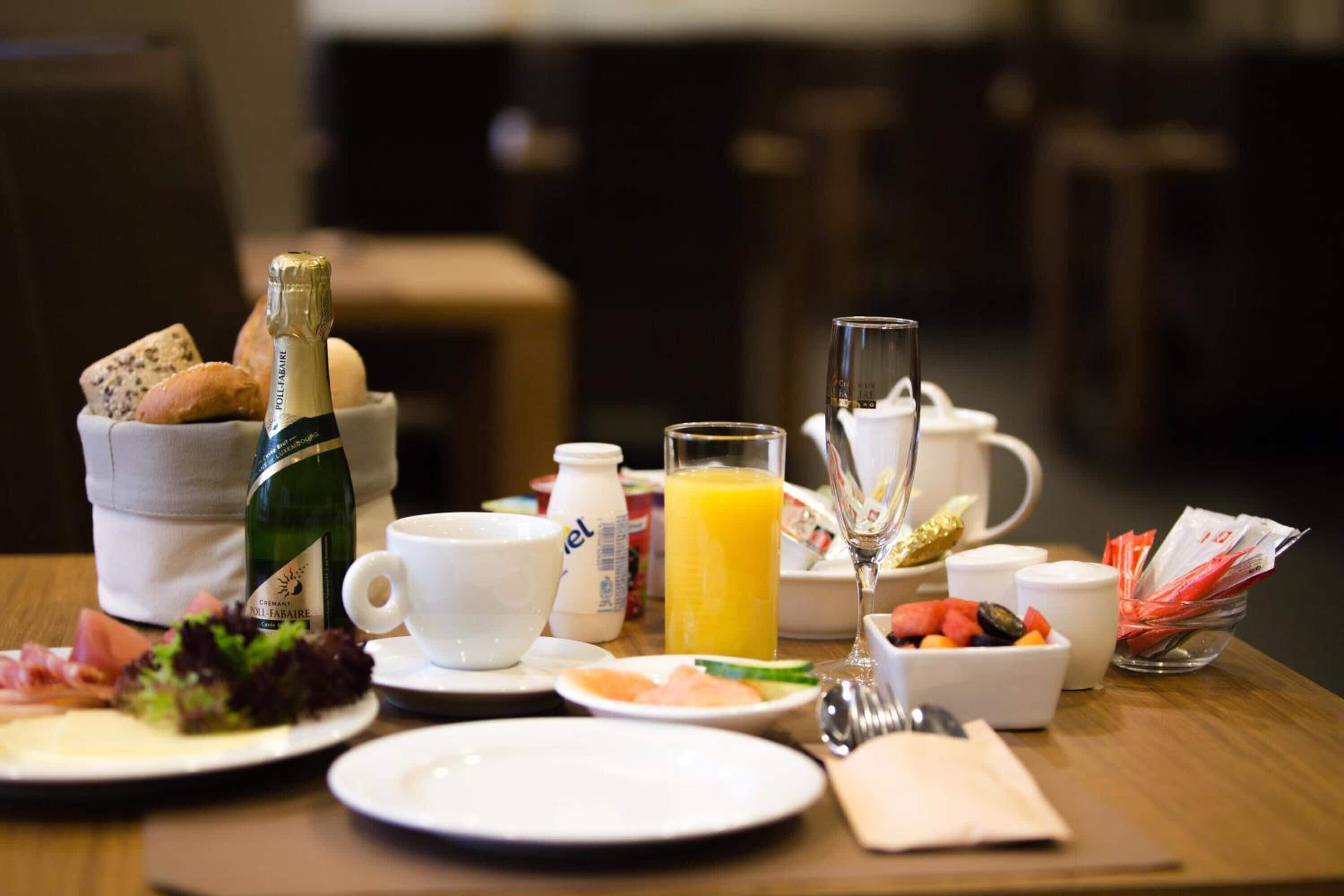 A breakfast table with a bottle of champagne, a glass of orange juice, and various breakfast items.