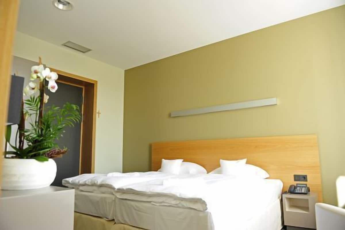 Une chambre d’hôtel moderne avec un grand lit, une table de chevet, une petite table et une plante en pot.