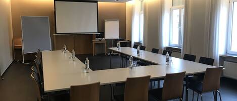 A conference room with a long table, chairs, a projector screen, and a whiteboard.