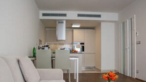 A modern living room with a sofa, a coffee table with a vase of flowers, and a view into a kitchen with a dining area. - Rezidence Muzeum (Prague)