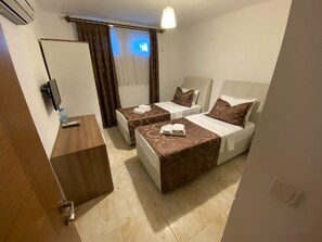 Una habitación de hotel con dos camas, un escritorio de madera, un televisor y un ventanal con cortinas.