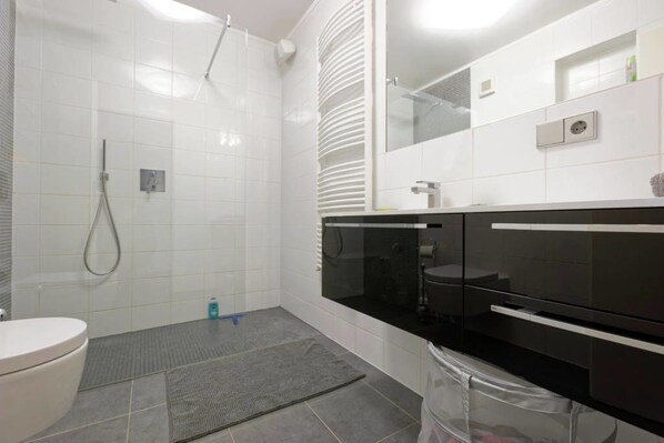 A modern bathroom with white tiles, a shower, a toilet, and a black vanity with a mirror. - Rooftop Luxembourg Ville (Luxembourg City)