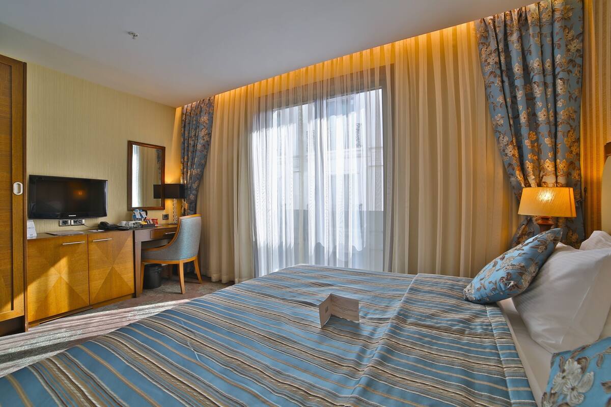 Une chambre d’hôtel avec un lit, un bureau, une télévision et des rideaux.
