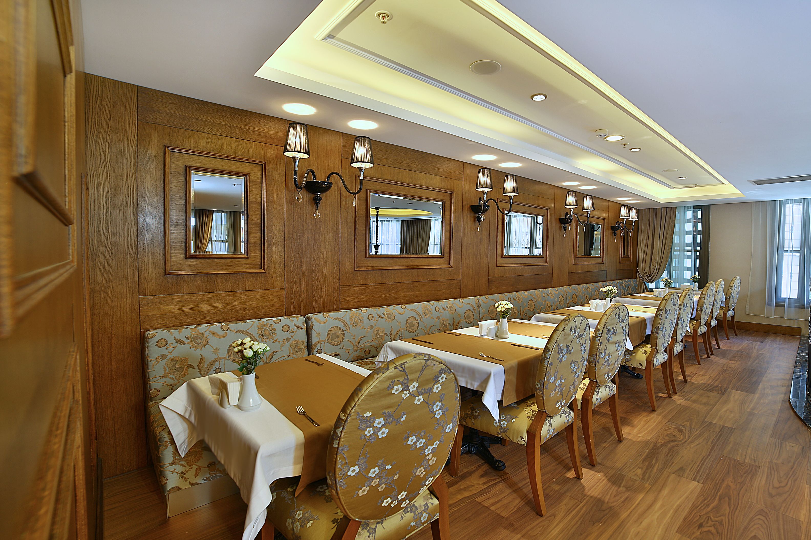A dining area with wooden paneling, mirrored walls, and a long table with chairs.