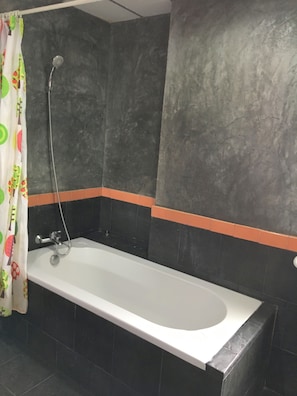A bathroom with a bathtub, shower, and dark tiled walls. - Taosha Suites (Kamala)