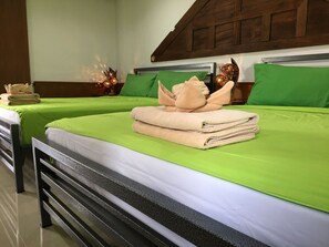 Two beds with green bedding, a wooden headboard, and a small decorative item on the nightstand. - Taosha Suites (Kamala)