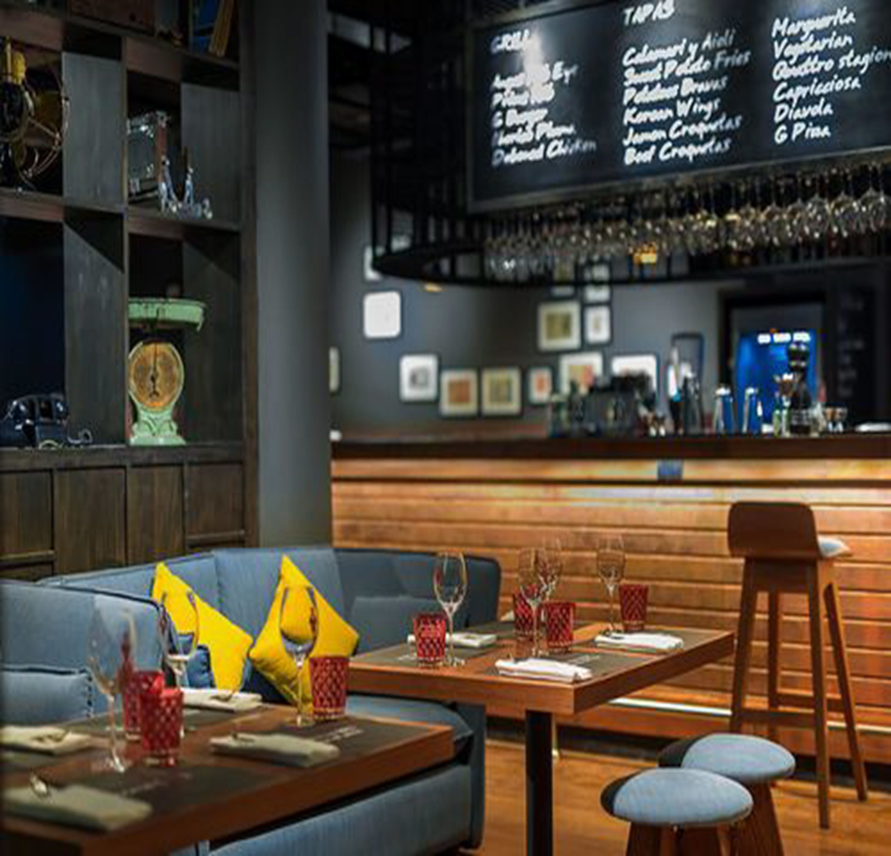 Interior de restaurante con barra, mesas de madera y un sofá azul.