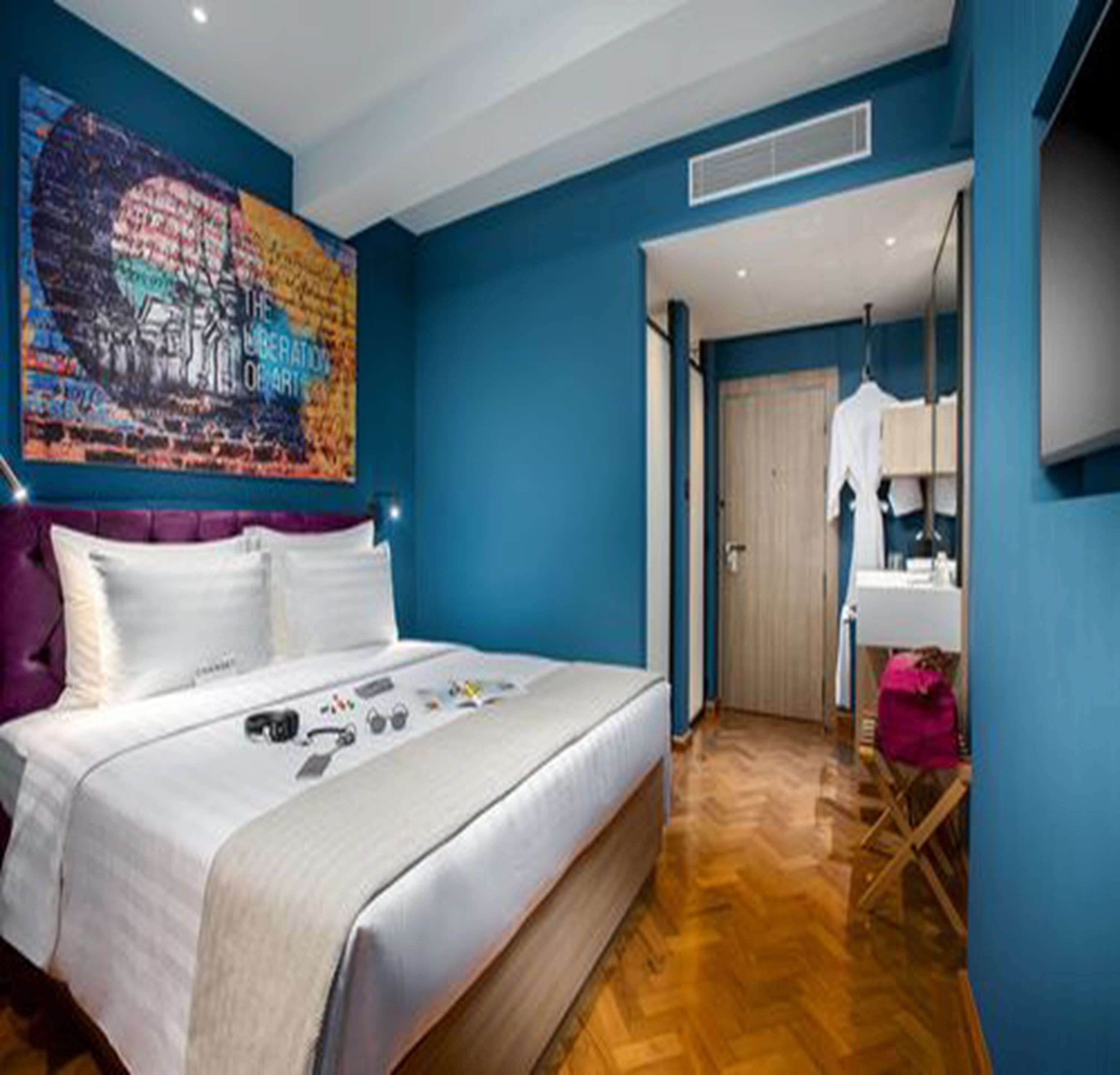 A modern bedroom with a large bed, a painting on the wall, and a bathroom visible through an open door.