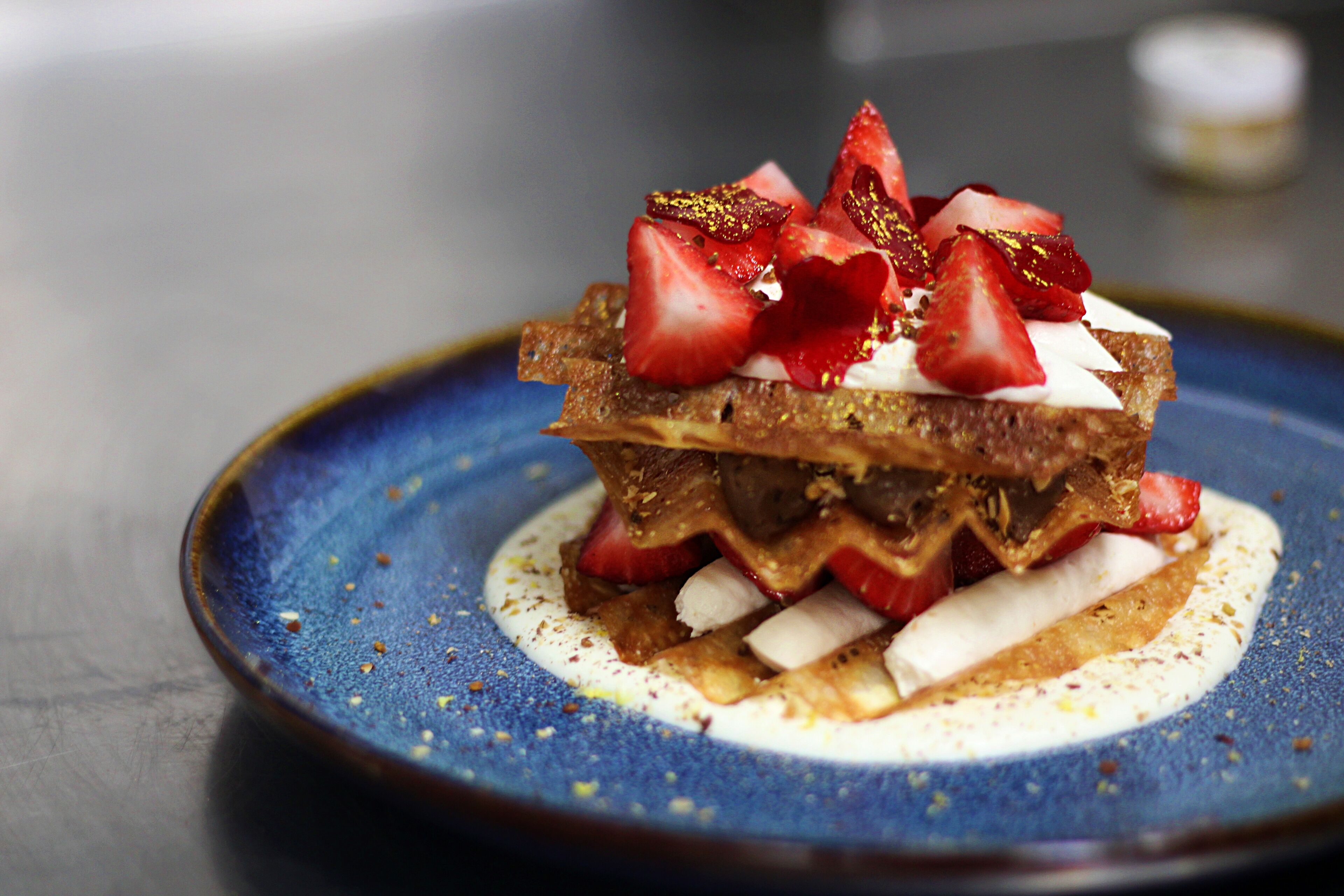 A dessert on a blue plate with strawberries and cream.