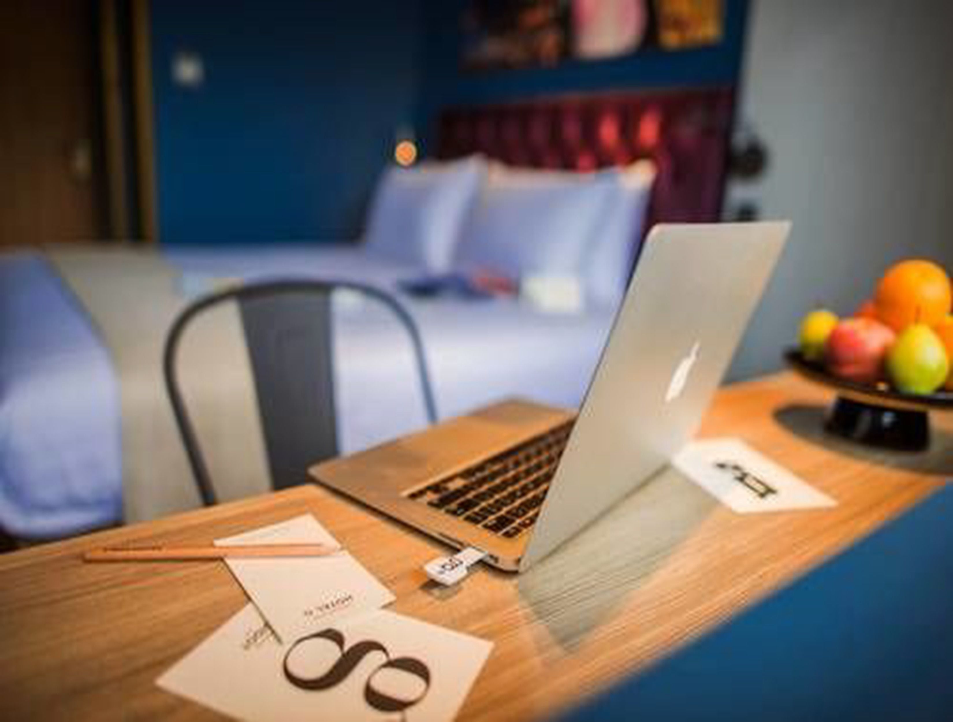 A laptop on a wooden desk with a bowl of fruit and a pair of glasses nearby.