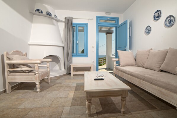 Una habitación con un sofá color beige, una silla de madera, una mesita pequeña y una puerta azul.
