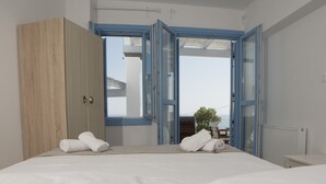 Un dormitorio con cama, dos toallas, un armario de madera y vistas a través de ventanas azules abiertas.