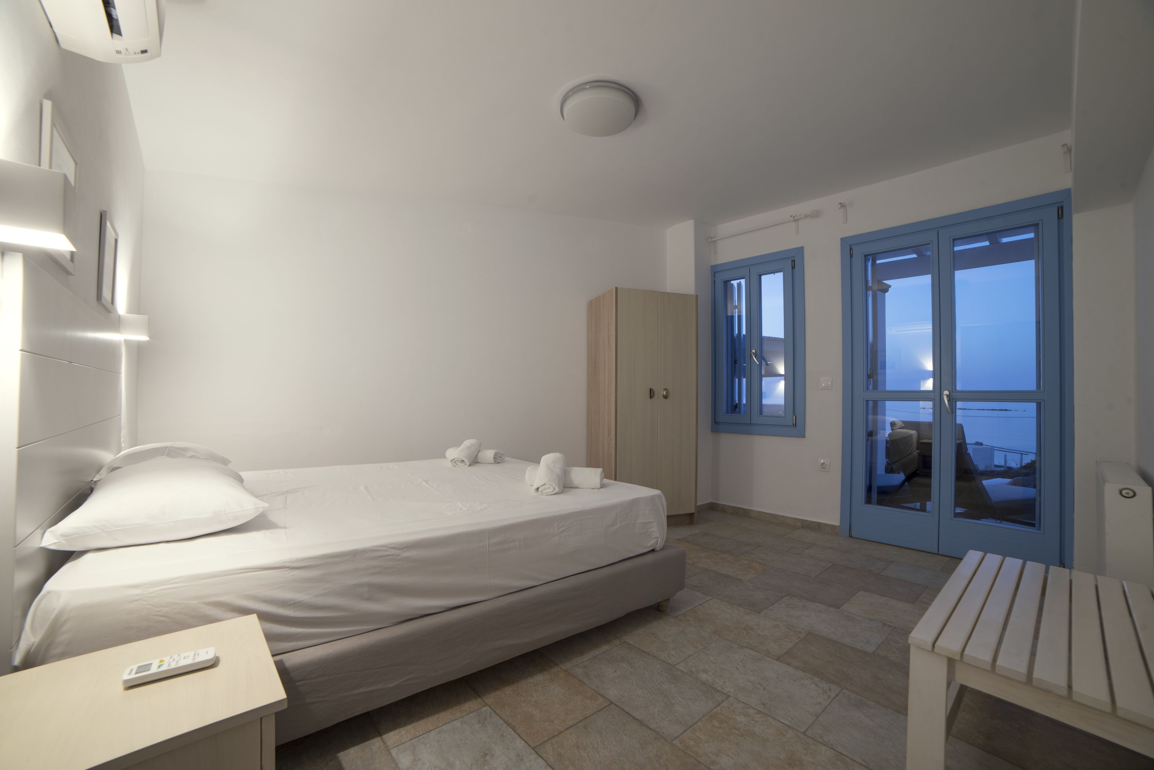 A hotel room with a bed, a bedside table, a wardrobe, and a view of the sea through a door.