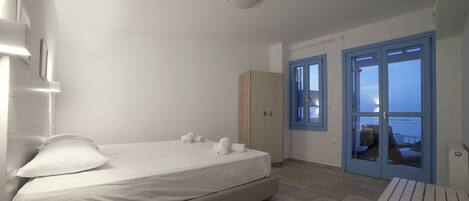 A hotel room with a bed, a bedside table, a wardrobe, and a view of the sea through a door.
