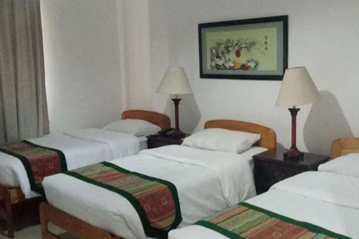 Ein Hotelzimmer mit vier Einzelbetten, jeweils mit Holz Kopfteilen und weißer Bettwäsche. Zwei Nachttische mit Lampen stehen bereit, und ein gerahmtes Bild hängt über den Betten an der Wand.
