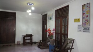 A room with a wooden door, a table, two chairs, a hanging light fixture, and a poster on the wall. - Thisara Guest Hotel Rooms (Kataragama)