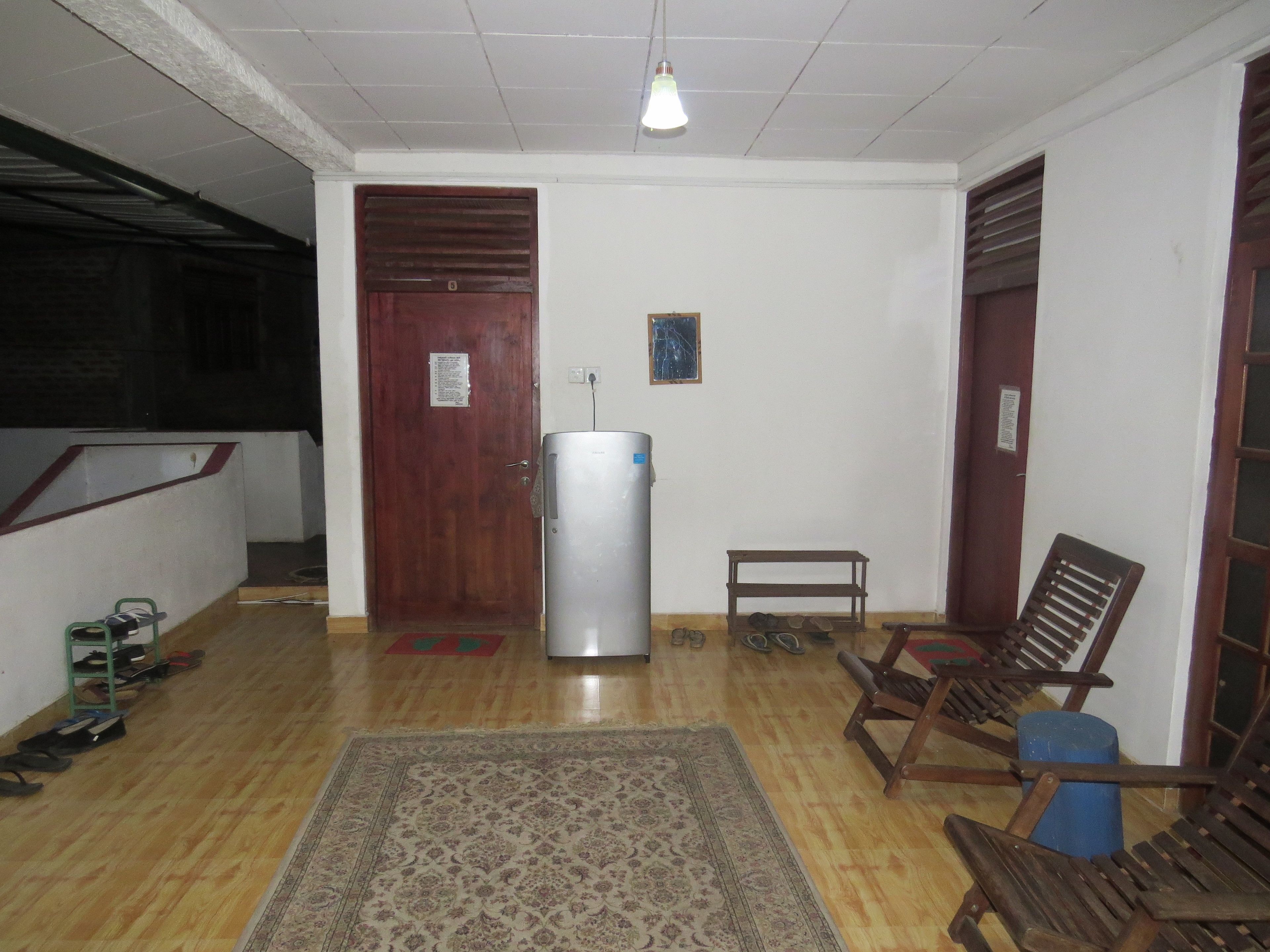 A hallway with a wooden door, a small table, and a chair. There is a rug on the floor and a light fixture on the ceiling.