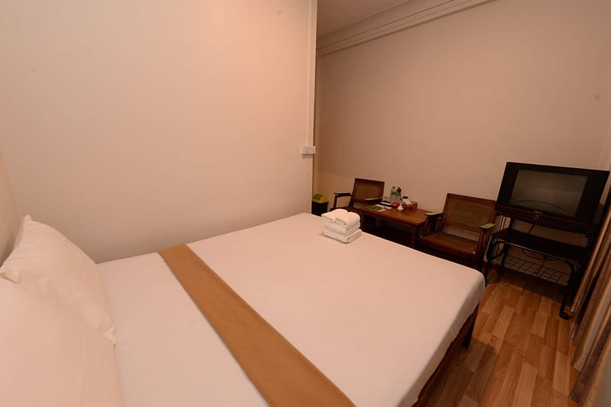 Hotellihuone, jossa on sänky, tuoli, pieni pöytä ja televisio.
