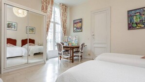 Une chambre d’hôtel avec deux lits, une table à manger avec des chaises, un grand miroir et des œuvres d’art accrochées aux murs.