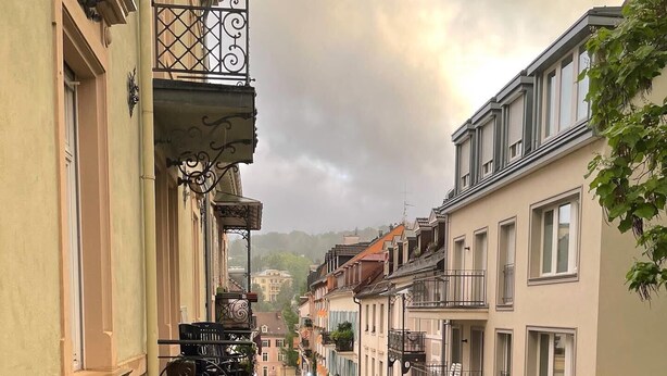 Eine schmale Stadtstraße, gesäumt von mehrstöckigen Gebäuden mit Balkonen und einer Mischung aus Wohn- und Geschäftsräumen.
