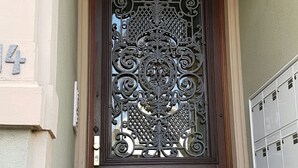 Eine dunkle Holztür mit aufwendiger Metallverzierung und einem kleinen Fenster darüber.
