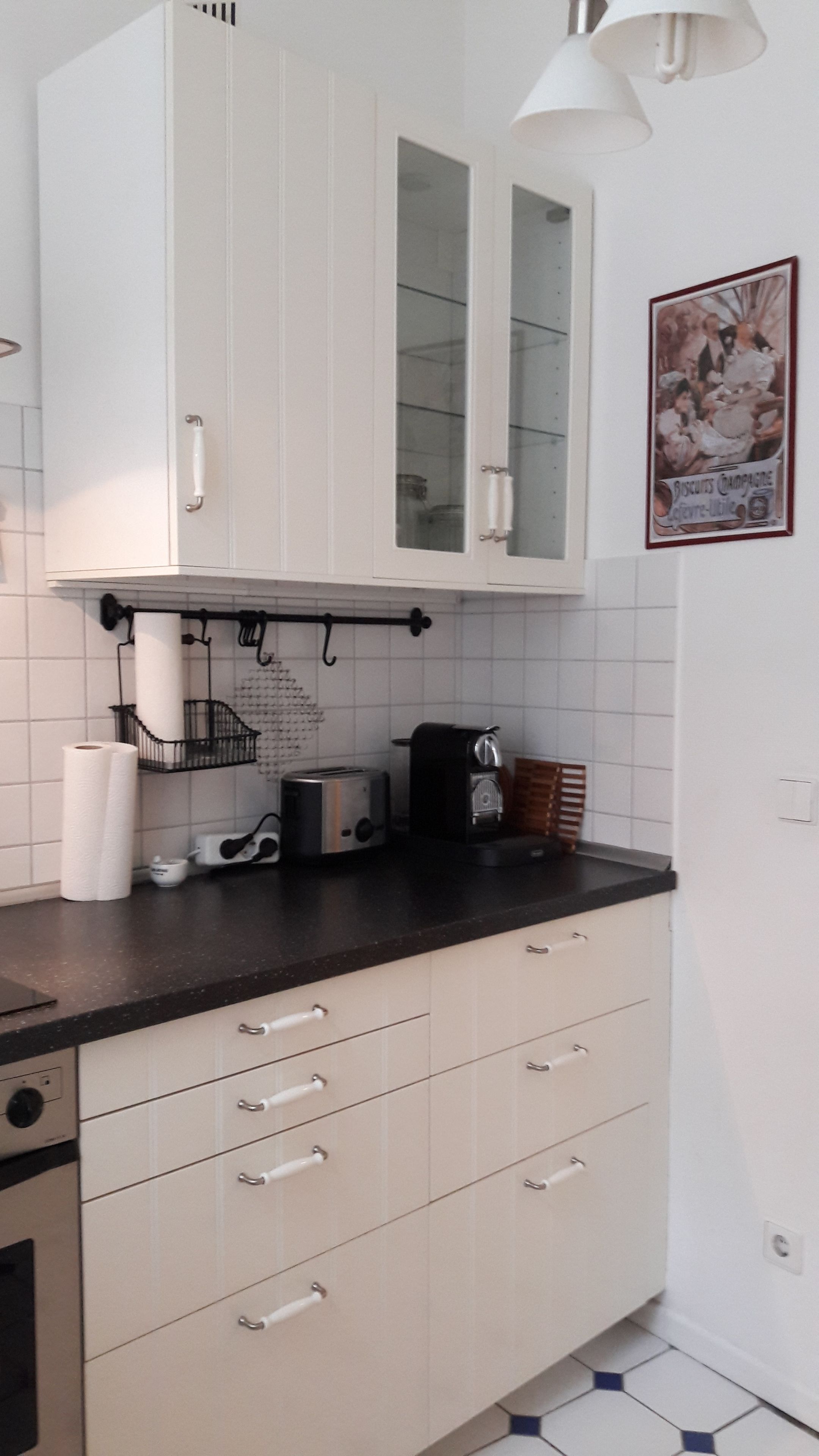 A kitchen with white cabinets, a black countertop, a toaster, and a hanging light fixture.