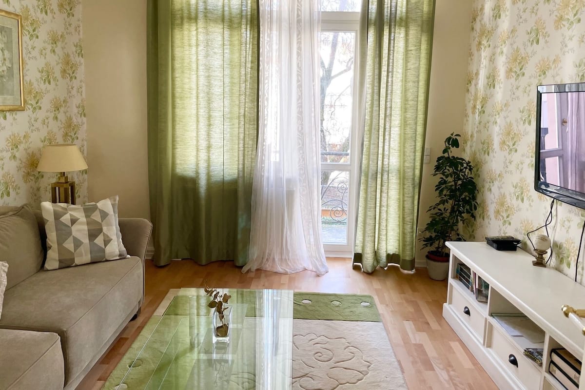 A living room with a sofa, a coffee table, a TV, and a window with curtains.