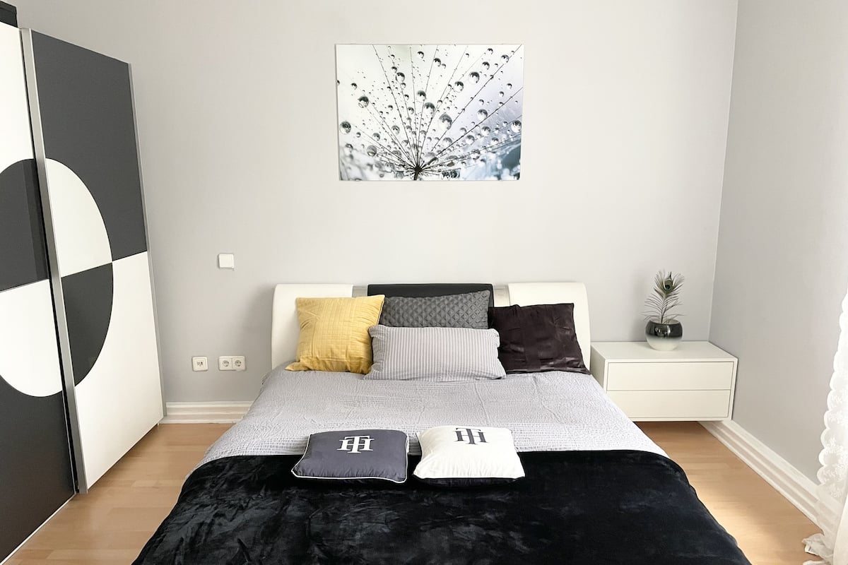 A modern bedroom with a bed, pillows, a nightstand, and a wall art piece.
