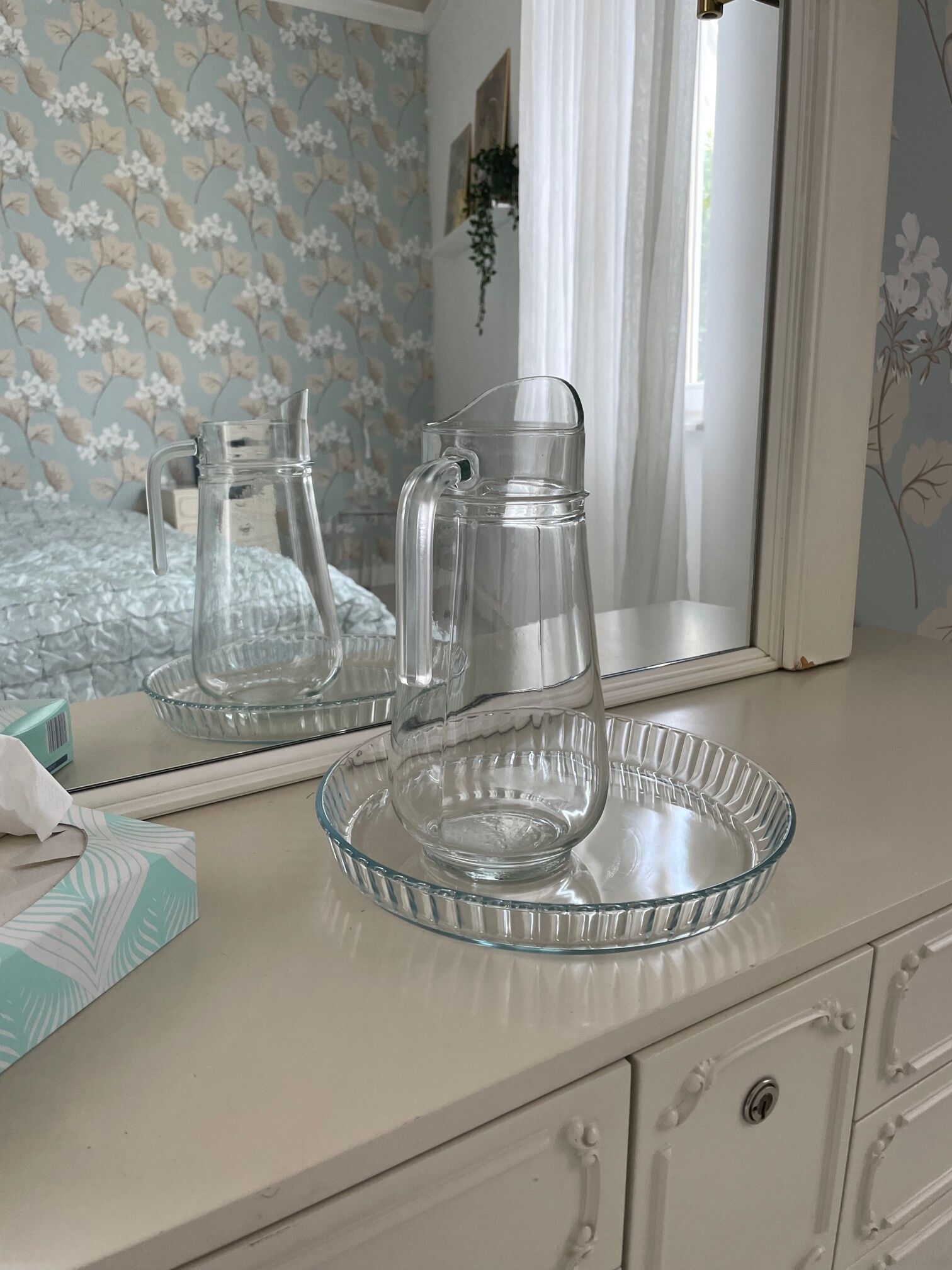 A bathroom vanity with a glass pitcher and a glass bowl on a tray.