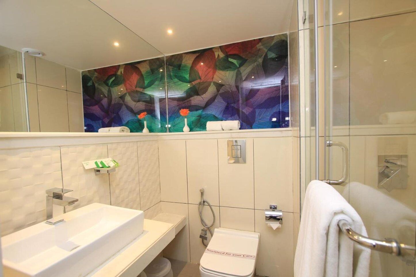 A modern bathroom with a glass shower enclosure, a white sink, and a towel rack.