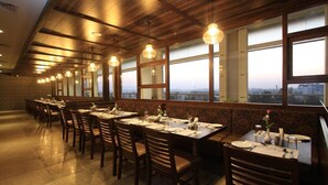 A restaurant with long tables and chairs, large windows, and a view of the city. - Icon Business by Bhagini  (Bengaluru)