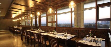 Ein Restaurant mit langen Tischen und Stühlen, großen Fenstern und Blick auf die Stadt.
