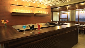 A bar area with a wooden counter, multiple glasses, and a view through large windows. - Icon Business by Bhagini  (Bengaluru)