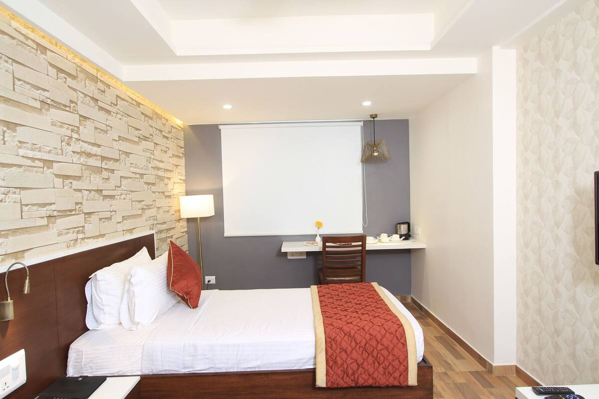 A hotel room with a bed, a desk, a chair, a TV, and a window.